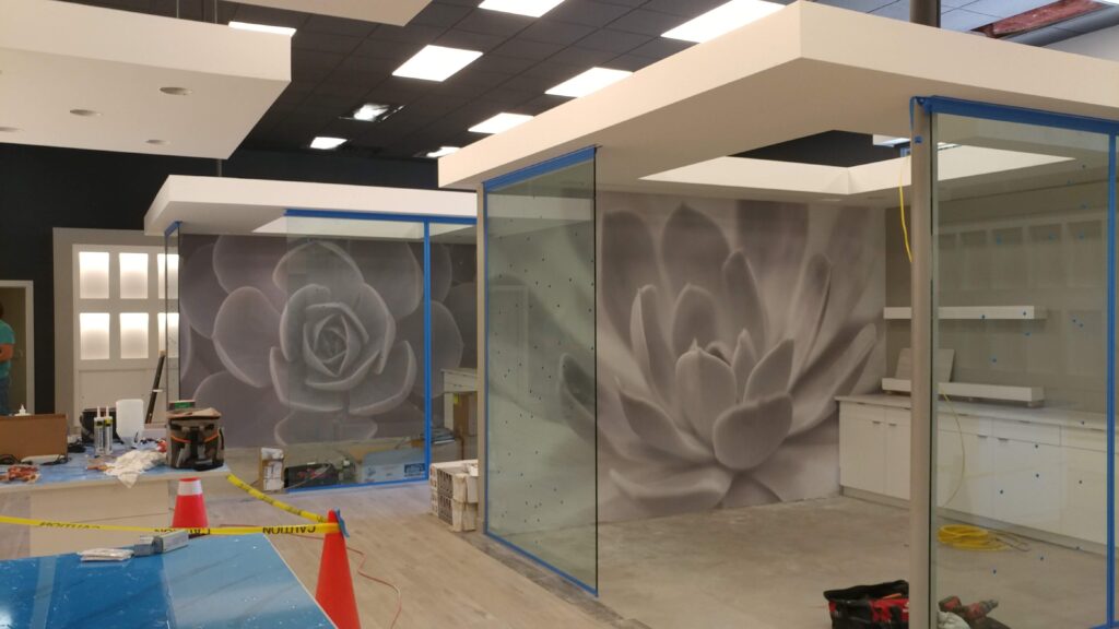 Interior of a construction site featuring large grayscale flower murals on glass walls, with equipment and caution tape present.