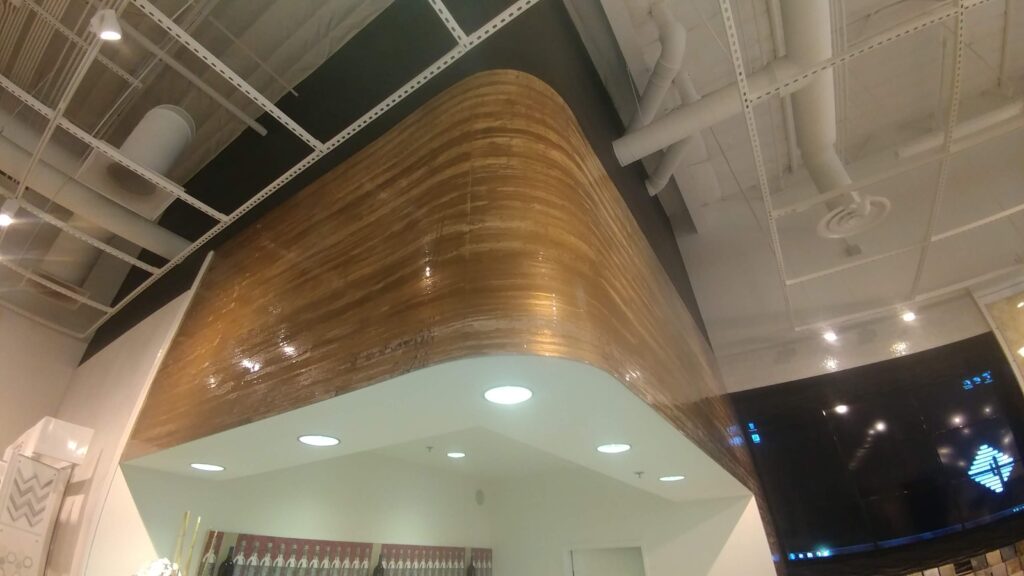 Interior of a modern building with a curved wooden panel ceiling, exposed ductwork, and recessed lighting.